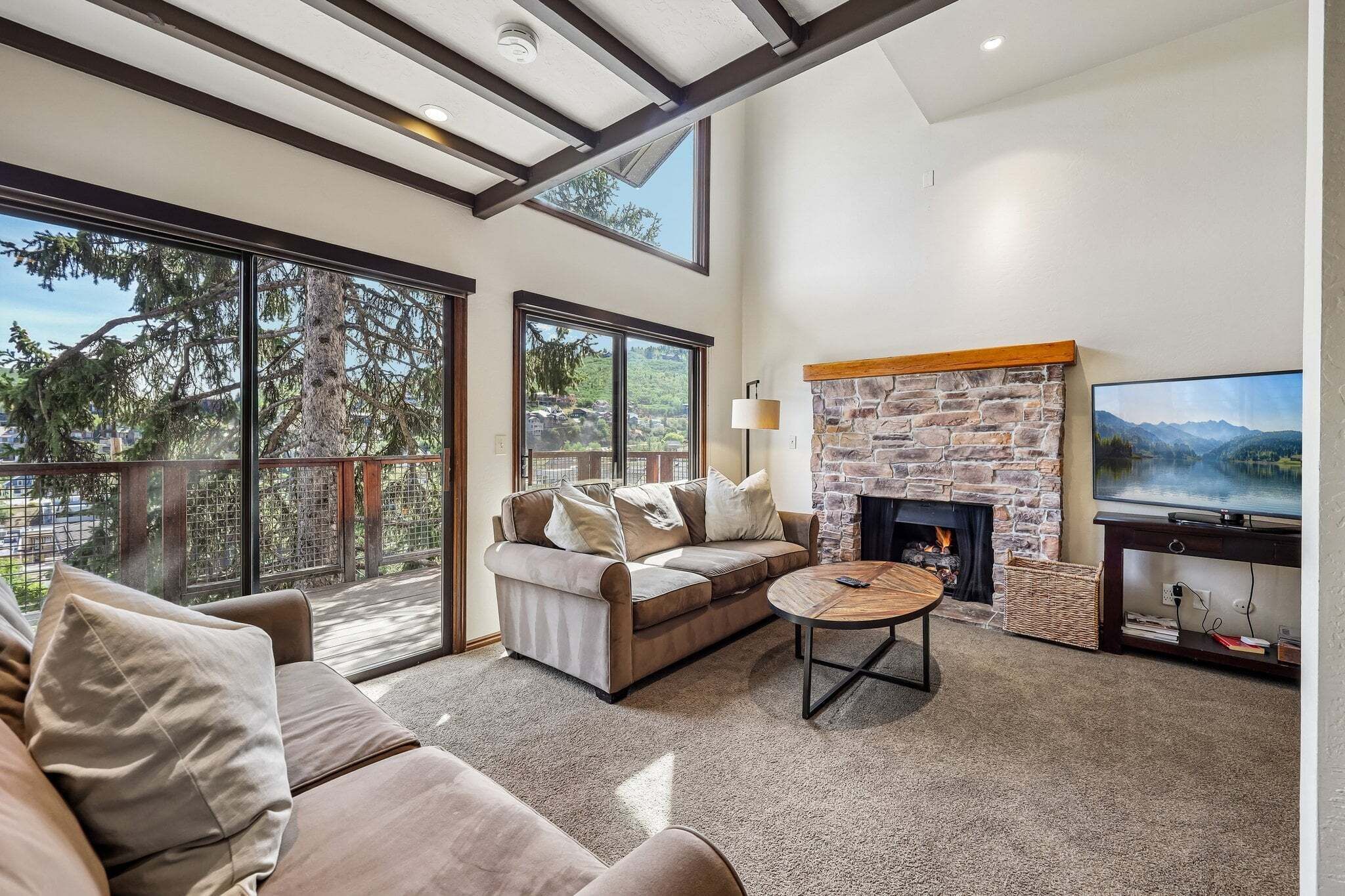 A modern living room with a stone fireplace, a large TV, and a sofa with cushions.
