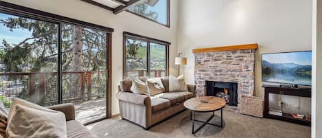 A modern living room with a stone fireplace, a large TV, and a sofa with cushions.