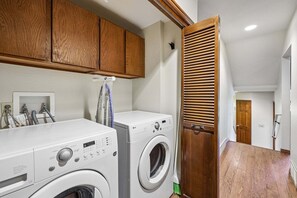 A laundry room with two white front-loading washing machines, wooden cabinets above, and a wooden door with horizontal slats. - Ski-In/Ski-Out* | 2 Blocks to Main Street | Private Sauna (Park City)