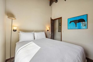 Une chambre à coucher avec un lit, deux lampes fixées au mur, une porte et un tableau représentant un cheval.