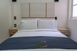 Cama com colcha azul escura, um emblema verde, cabeceira branca e duas mesas de cabeceira com abajures.
