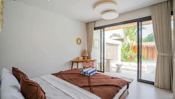 Un dormitorio con una cama grande, una mesita de noche con lámpara y vistas a un jardín a través de puertas corredizas de vidrio.