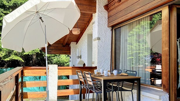 Een terras buiten met een tafel, stoelen en een witte parasol.