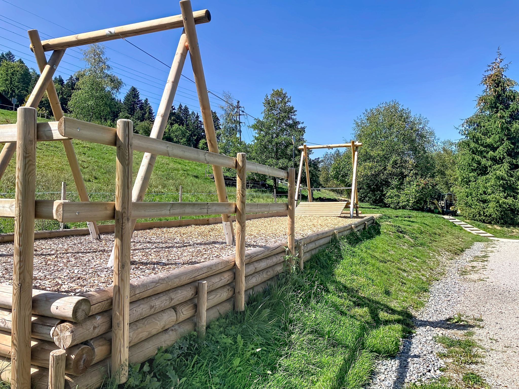 A wooden fence with a gravel path and greenery in the background.