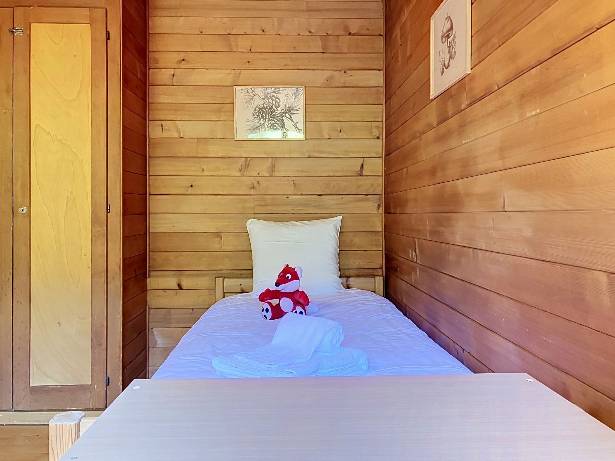 Quarto de cabana de madeira com uma cama, um travesseiro, um brinquedo de pelúcia e um quadro na parede.
