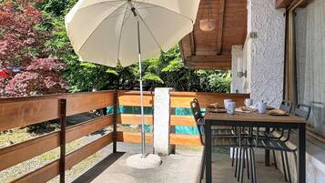 A patio with a table and chairs, a wooden bench, a hanging pot, and a view of greenery.