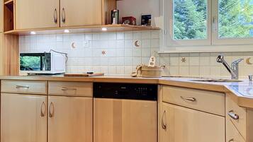 A kitchen with wooden cabinets, a microwave, a dishwasher, and a window with a view of trees.