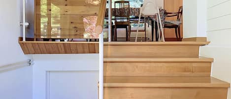 Eine Holztreppe mit Glastrennwand führt zu einem Essbereich mit Tisch und Stühlen.