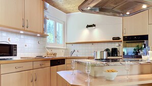 Een keuken met houten kastjes, een magnetron, een spoelbak en een aanrecht met twee wijnglazen en een schaal chips.