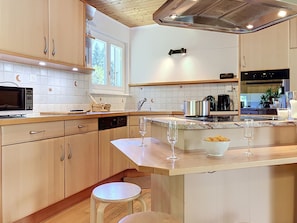 Una cocina con armarios de madera, microondas, fregadero y encimera con dos copas de vino y un cuenco de patatas fritas.
