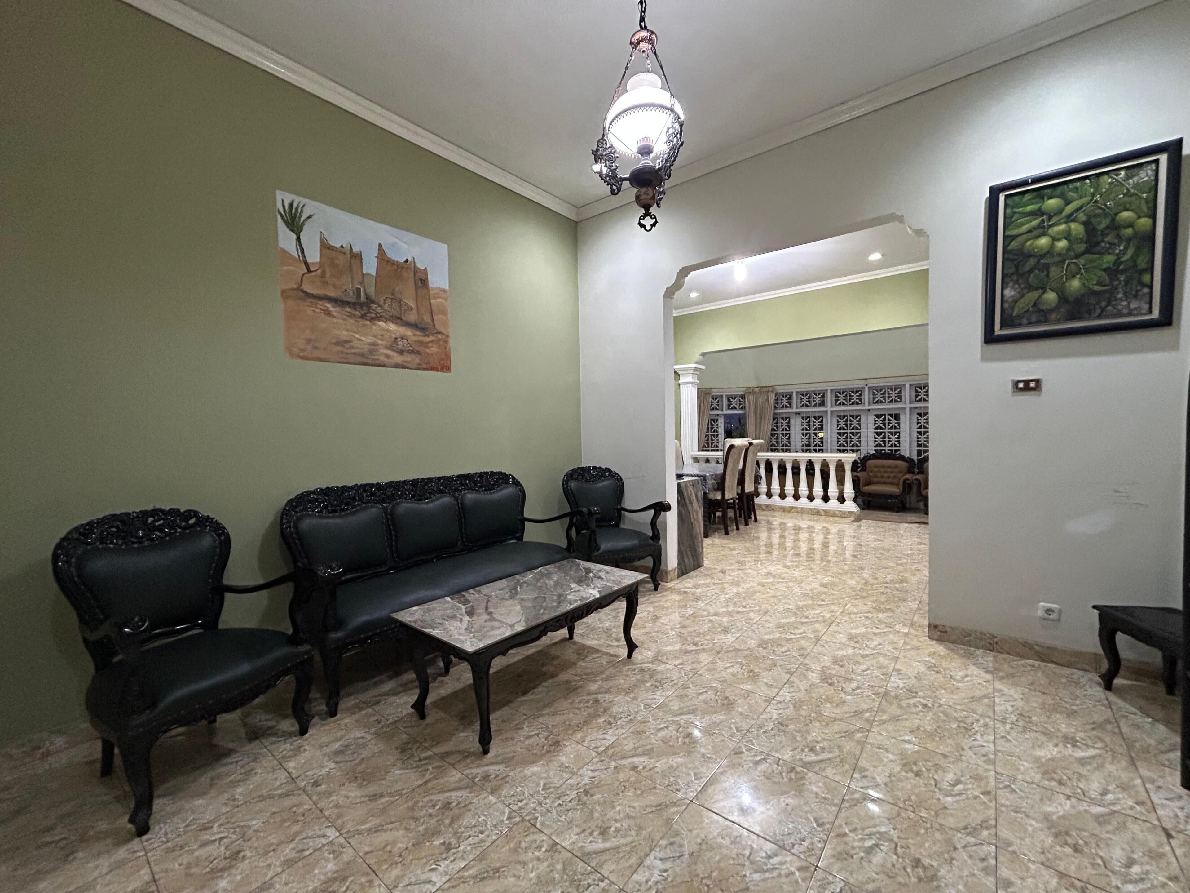 Amplia sala de estar con piso de mármol, un conjunto de sofás, una mesa de comedor y una araña.