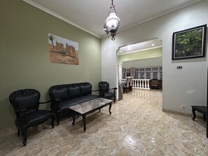A spacious living area with a marble floor, a sofa set, a dining table, and a chandelier.