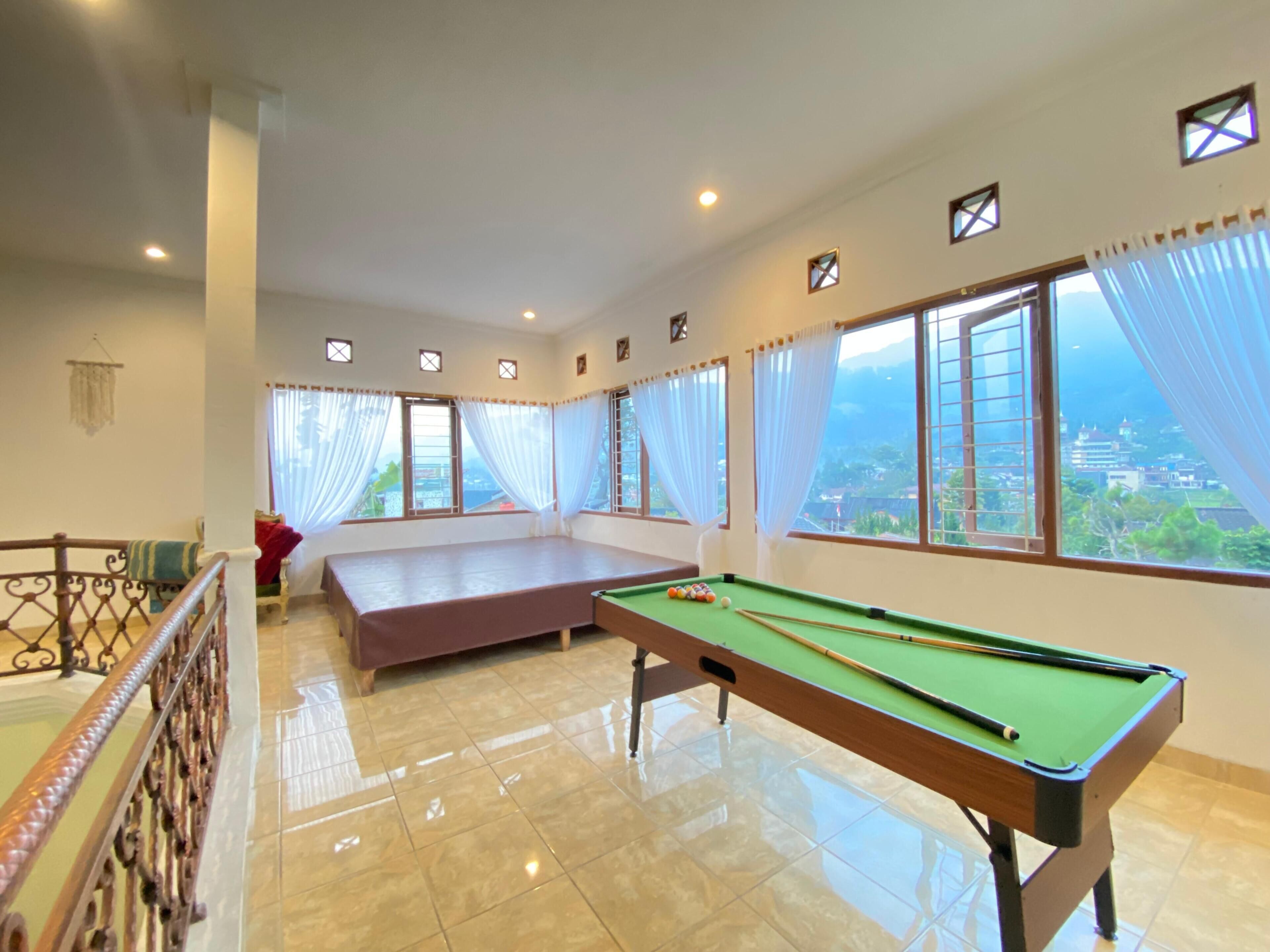 A room with a pool table, a bed, and large windows with curtains.