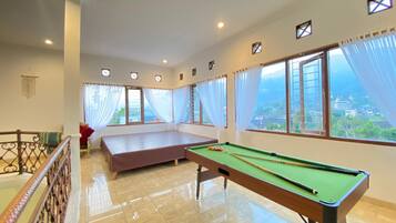 A room with a pool table, a bed, and large windows with curtains.