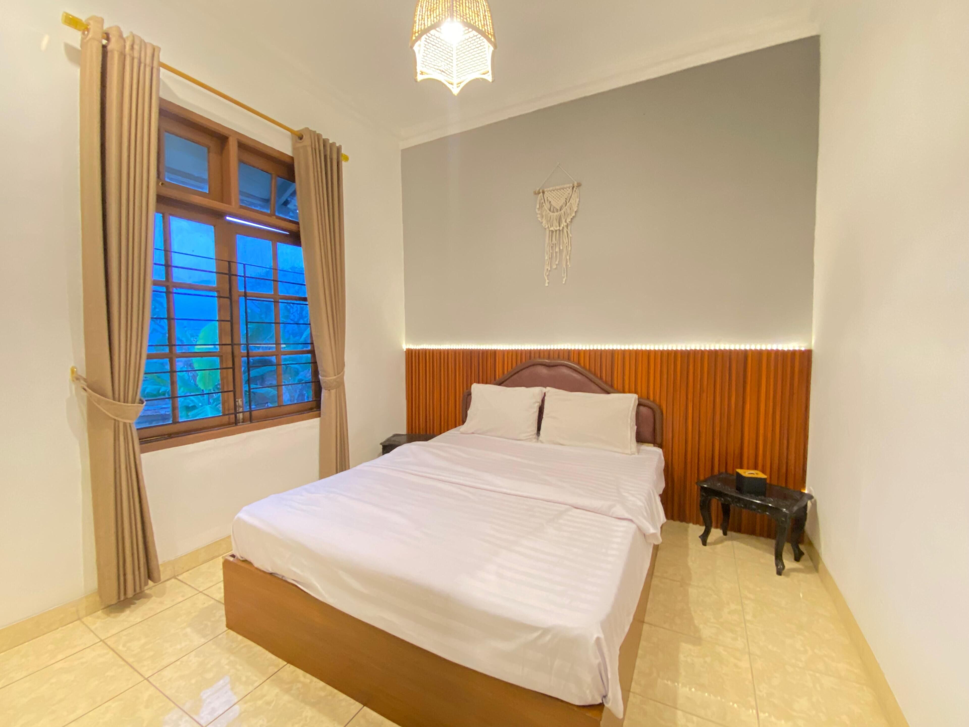 Un dormitorio con cama, mesita de noche, decoración de macramé en la pared y ventana con cortinas.