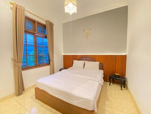 A bedroom with a bed, a nightstand, a wall-mounted macrame decoration, and a window with curtains.