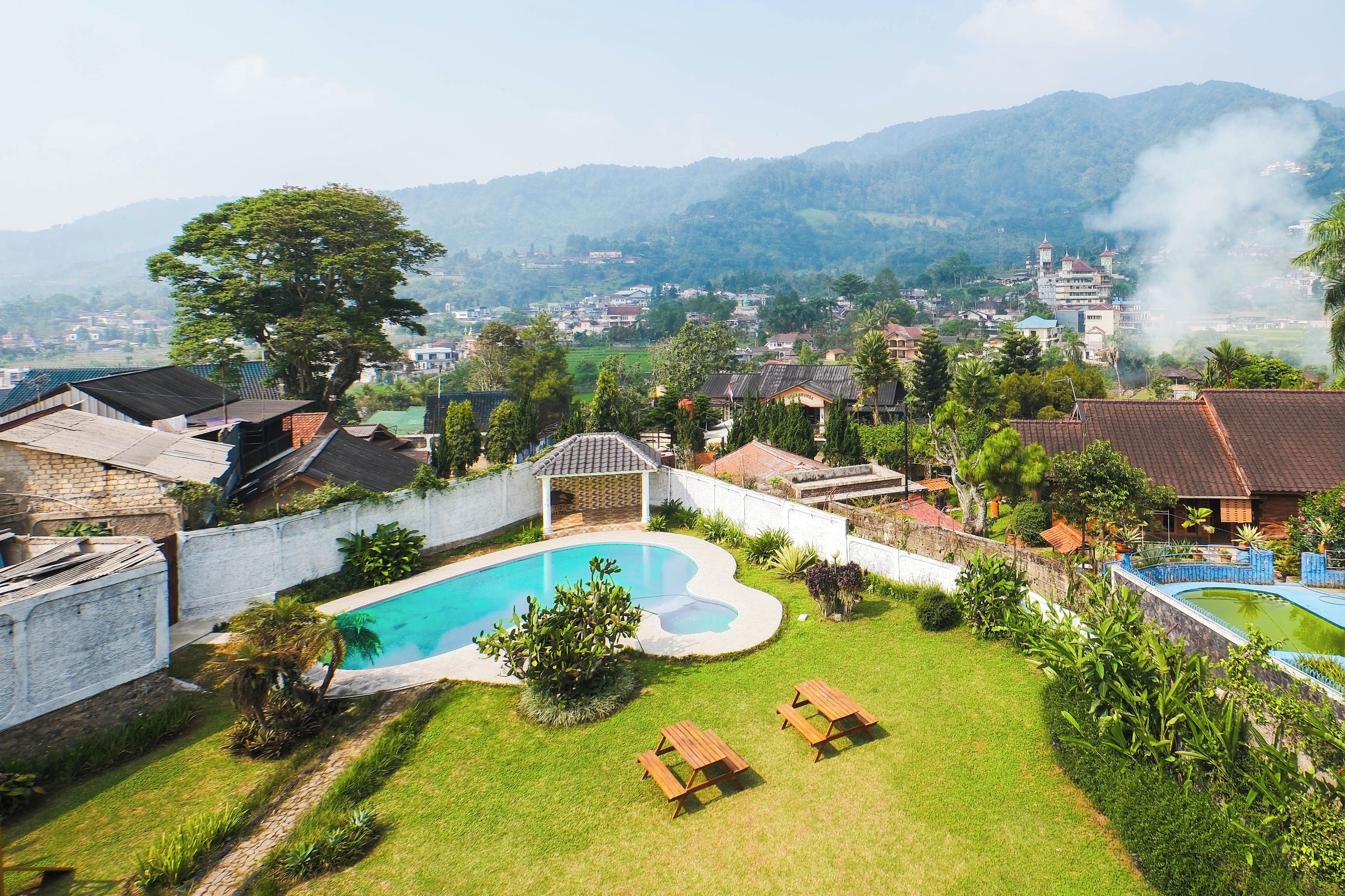A residential area with a swimming pool, green lawns, and houses with red-tiled roofs.