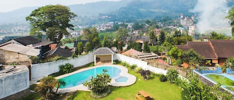 A residential area with a swimming pool, green lawns, and houses with red-tiled roofs.