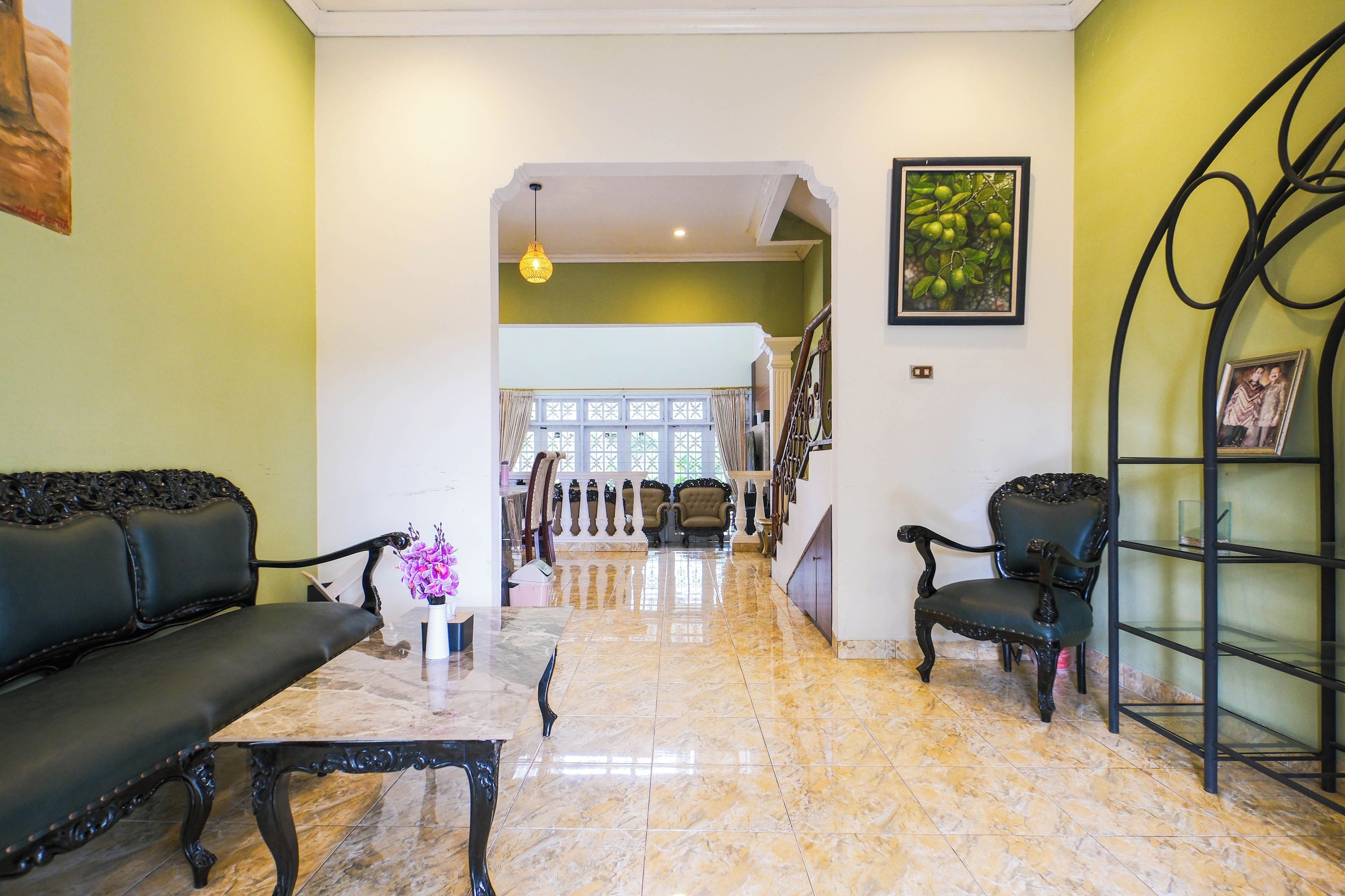 A spacious living area with a marble floor, a black sofa, a black armchair, and a small table with a vase of flowers.