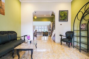 Amplia sala de estar con piso de mármol, un sofá negro, un sillón negro y una pequeña mesa con un jarrón de flores.