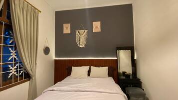 A bedroom with a bed, a bedside table, a mirror, and a window with curtains.