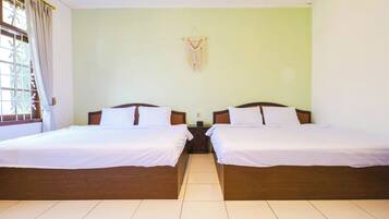 Ein Hotelzimmer mit zwei Betten, einem fensterbelaubten Fenster, einer wandhängenden Makramee-Dekoration und einem gefliesten Boden.