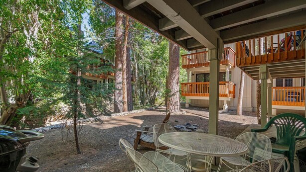 Un área de patio al aire libre con una mesa redonda y sillas, rodeada de árboles y un edificio con balcones.