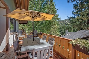 Une terrasse extérieure avec une table et des chaises, un grand parasol et une vue sur les arbres et les collines.