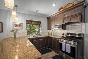 A kitchen with granite countertops, dark wooden cabinets, stainless steel appliances, and a window with a view of greenery. - 1366 Zurich | 3BR/3.5BA Incline Village (Incline Village)