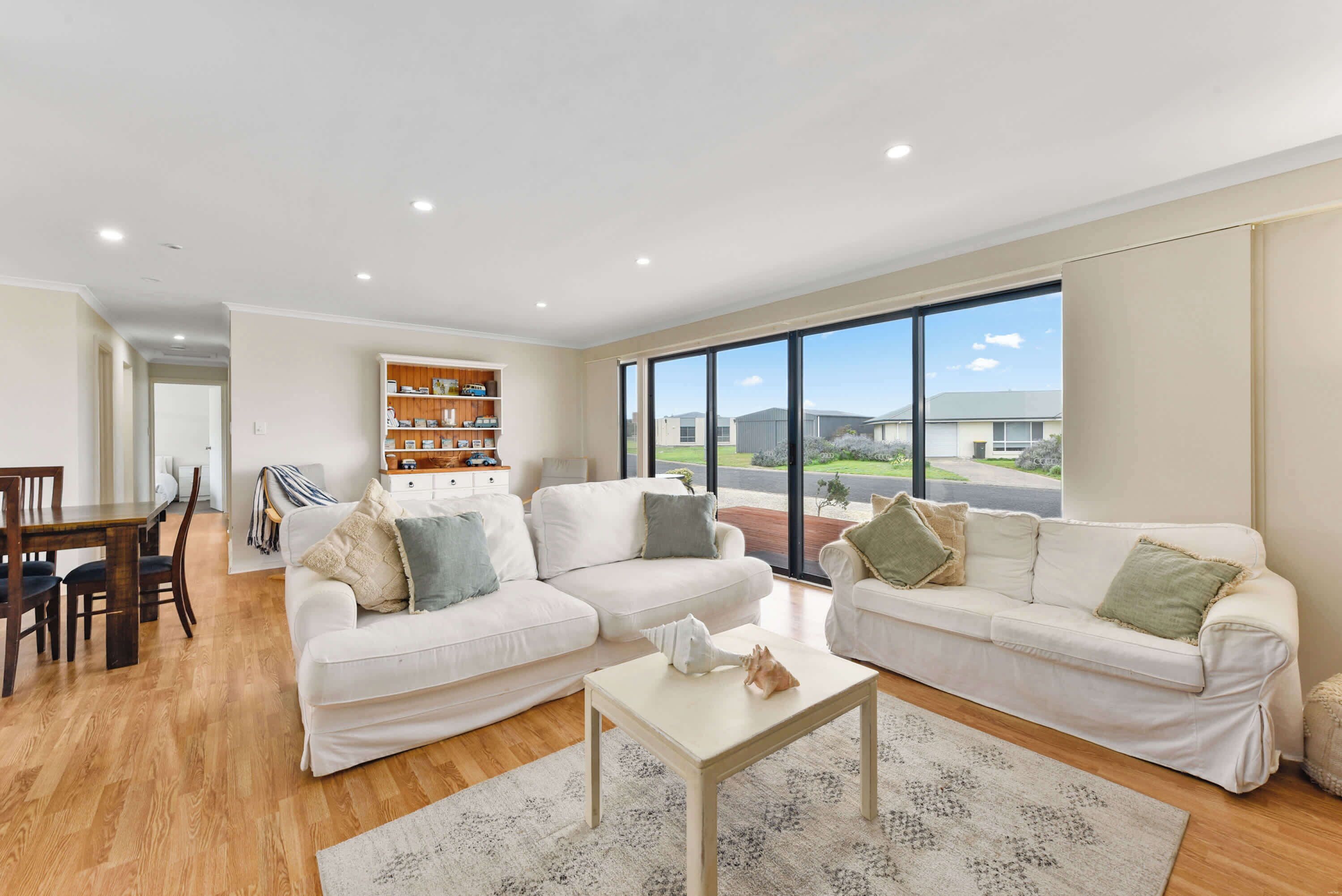 A spacious living room with two white sofas, a coffee table, and a wooden bookshelf.
