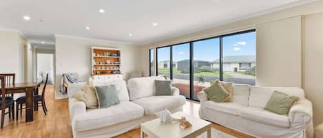 A spacious living room with two white sofas, a coffee table, and a wooden bookshelf.