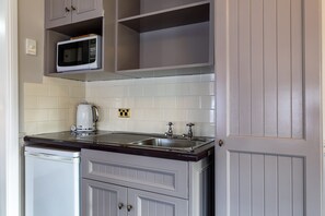 Una cocina compacta con microondas, hervidor y pileta.