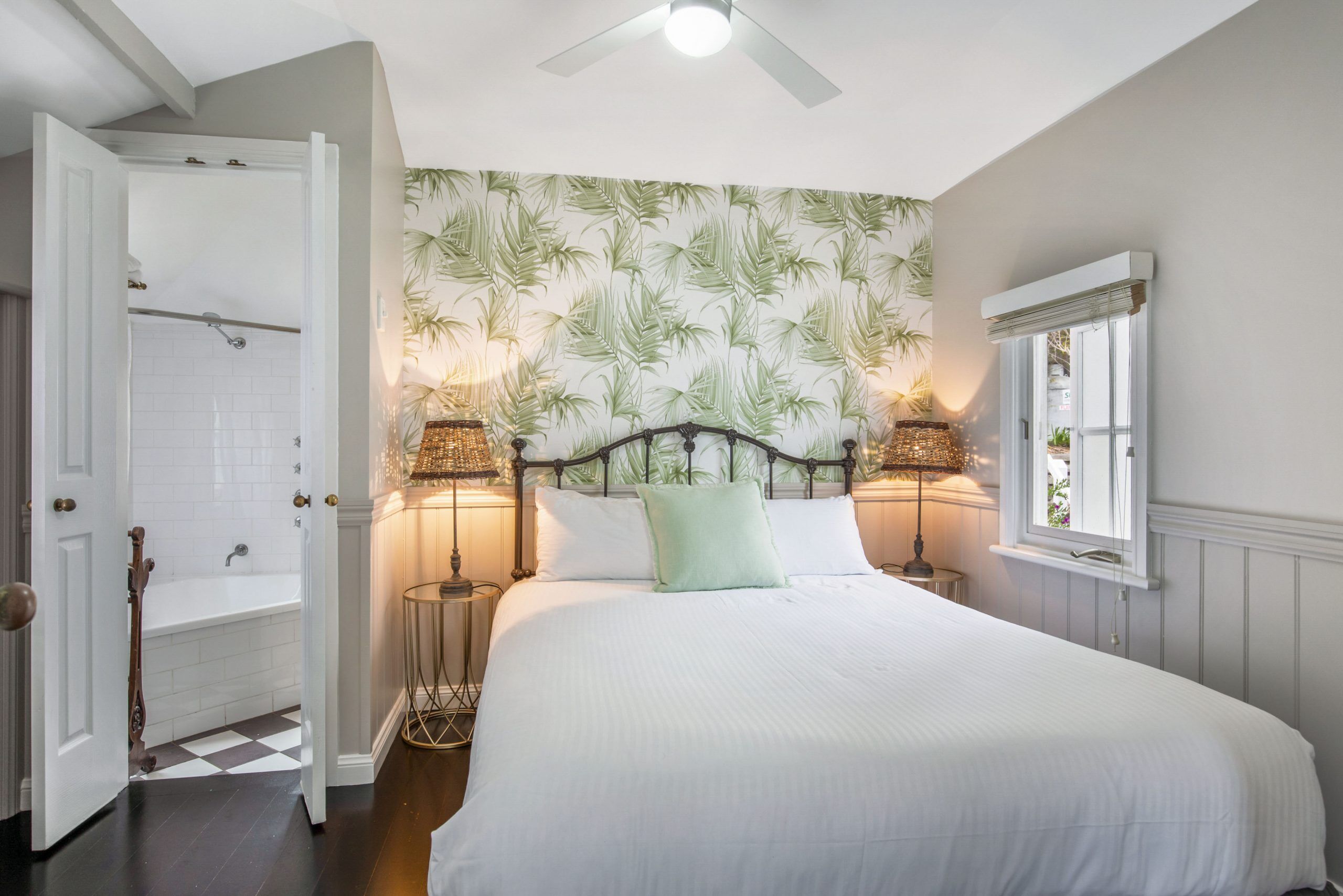 A bedroom with a bed, two bedside lamps, a window, and a door leading to a bathroom.
