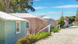 A row of single-story houses with metal roofs, a gravel driveway, and a clear sky.