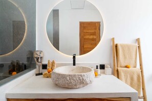 A bathroom with a round mirror, a stone sink, and a wooden door. - Villa Puligny (Tibubeneng)