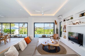 A modern living room with a large TV, comfortable seating, and a view of a swimming pool. - Villa Victorine (Canggu)