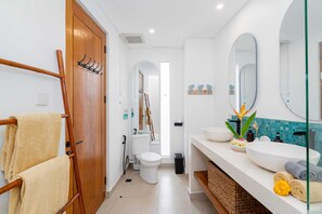 A modern bathroom with a wooden door, a towel rack, a toilet, a bidet, and a large mirror. - Villa Casa Diamanti (Tumbak Bayuh)