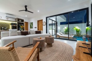 Ein modernes Wohnzimmer mit einem großen Sofa, einem Couchtisch und Blick auf einen Swimmingpool.
