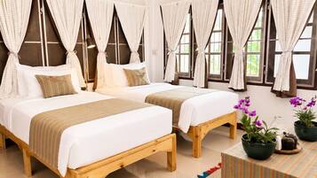 A hotel room with two beds, a wooden floor, and large windows with curtains.