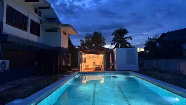 Une piscine dotée d’une terrasse carrelée, entourée d’un bâtiment à toit plat et aux grandes fenêtres.
