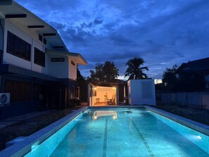 Una piscina con suelo de baldosas, rodeada por un edificio de techo plano y grandes ventanales.