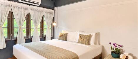 A bedroom with a bed, curtains, a bedside table with a plant, and an air conditioning unit.