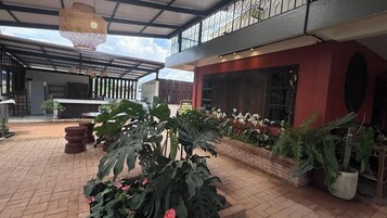 Un patio exterior con zona de estar cubierta, plantas en macetas y suelo de ladrillo.