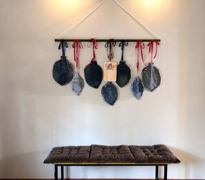 Un perchero de pared con varios objetos, incluyendo una placa de madera y algunas prendas vaqueras. Abajo, un banco tapizado descansa sobre un soporte de madera.