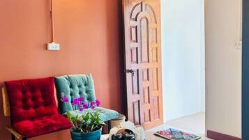 Um quarto com uma cadeira vermelha, uma cadeira azul-esverdeada, uma tigela azul com uma planta, um tabuleiro com uma chaleira e uma porta de madeira.