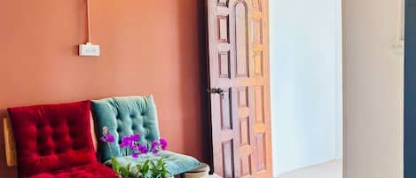 A room with a red chair, a teal chair, a blue bowl with a plant, a tray with a teapot, and a wooden door.