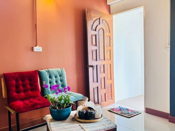 A room with a red chair, a teal chair, a blue bowl with a plant, a tray with a teapot, and a wooden door.