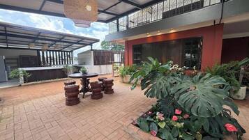 Un espace extérieur aménagé en patio, avec une table et des chaises, entouré de plantes en pot et d’une grande plante à feuilles luxuriantes.