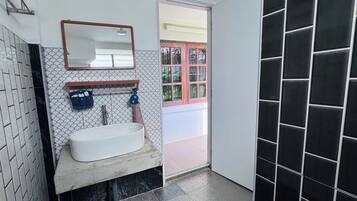 Un baño con lavamanos blanco, un espejo y una ventana con marco rojo.
