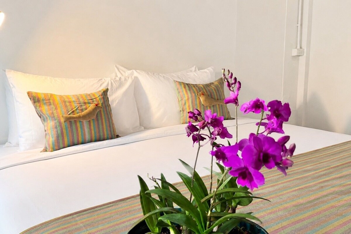 A hotel room with a bed, pillows, a lamp, and a potted orchid plant.
